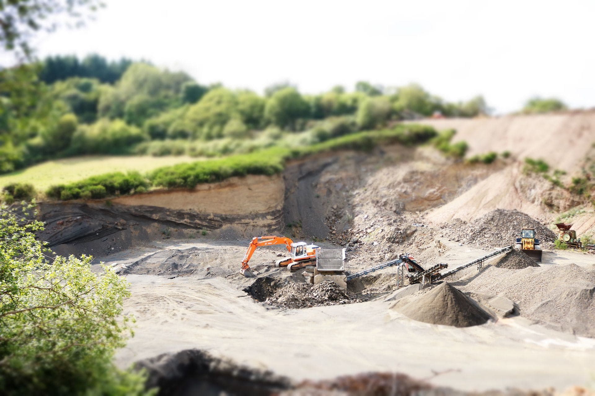 Kieswerk mit Bagger und Halden, dahinter Wald — Abbaufläche ohne Zaun