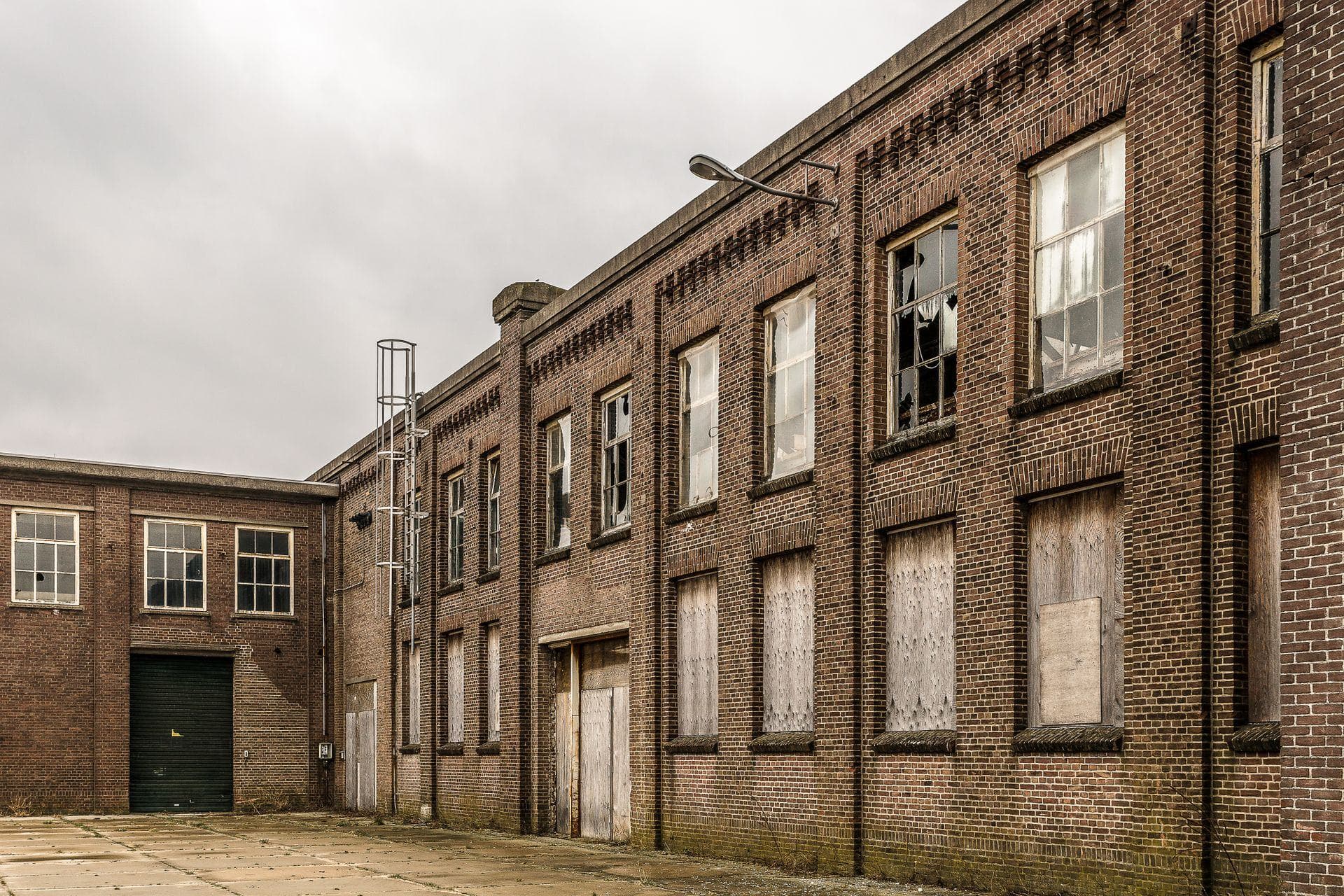 Leerstehendes Backsteingebäude mit vernagelten Fenstern und leerem Hof